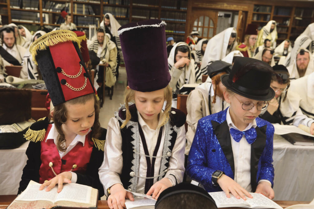 Three Jewish boys, dressed in costumes, read the Megillah (Book of Esther) in a synagogue during Purim. (Credit: Flash90)