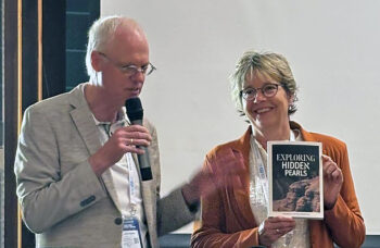 Jacob spreekt door microfoon en Hennie houdt engelse vertaling Exploring Hidden Pearls vast