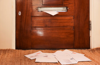 Wooden door with mail slot and many envelopes indoors